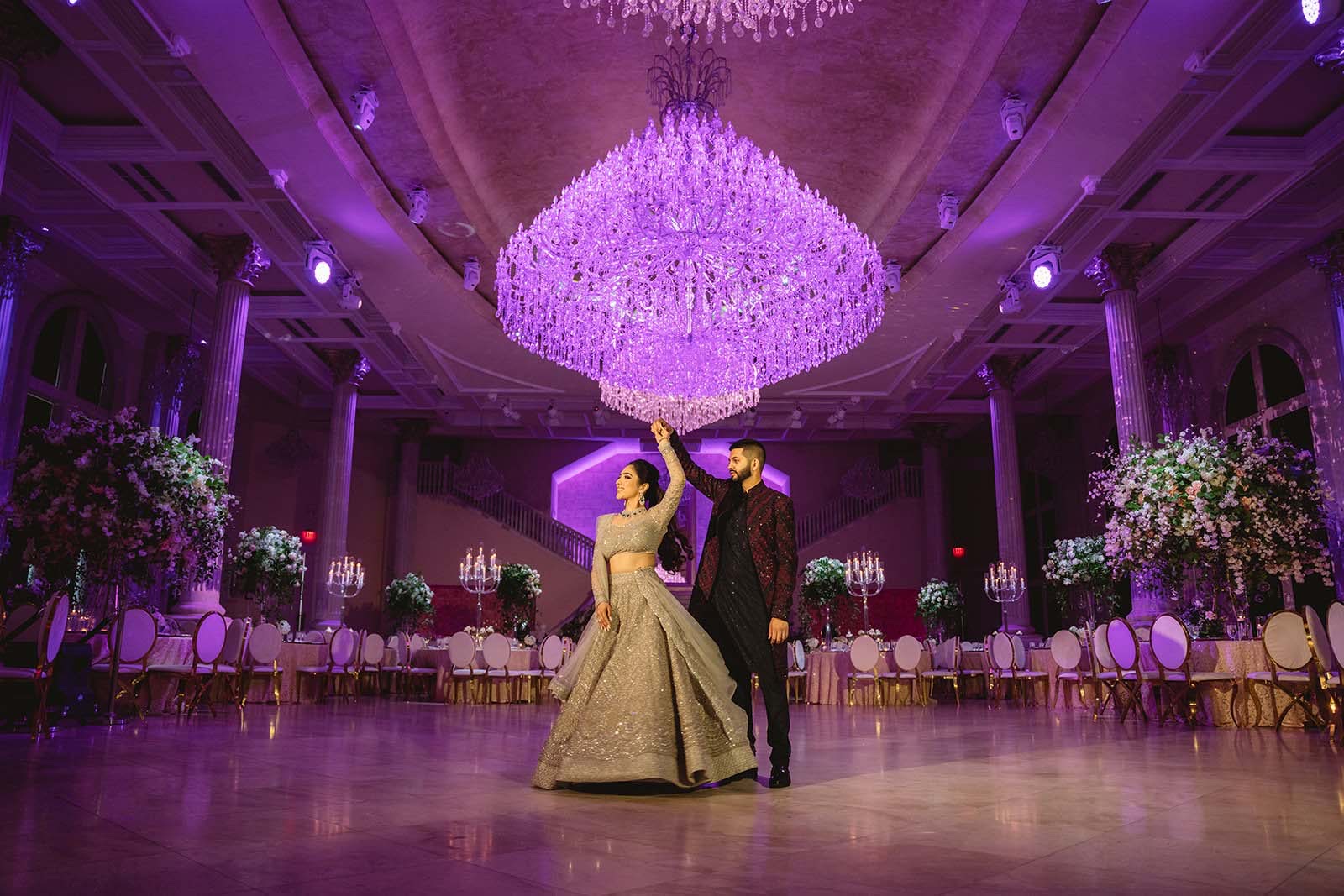 Couple dancing under a glowing crystal chandelier in a grand purple-lit ballroom
