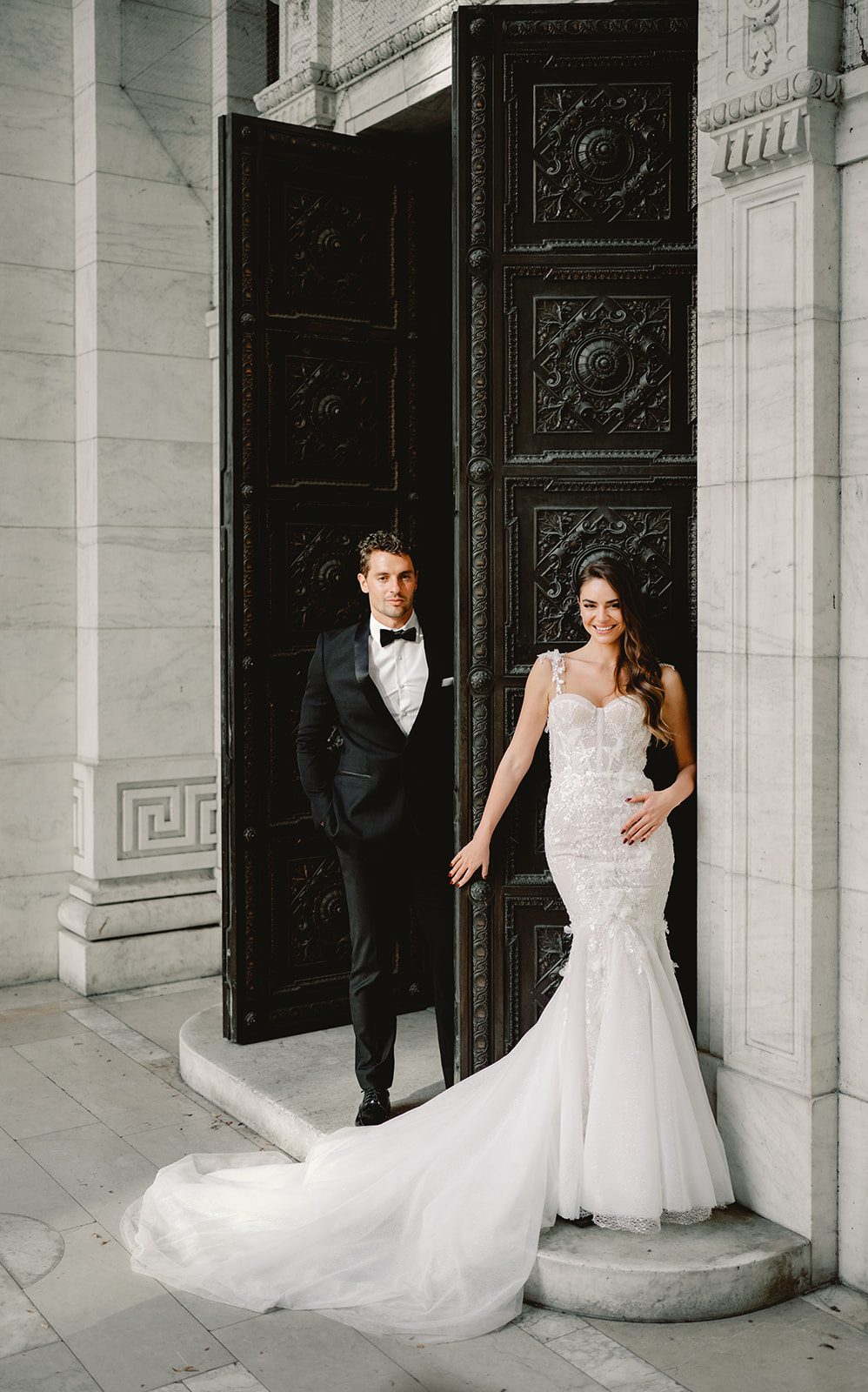 Bride and groom posing in front of ornate bronze doors at a grand stone building